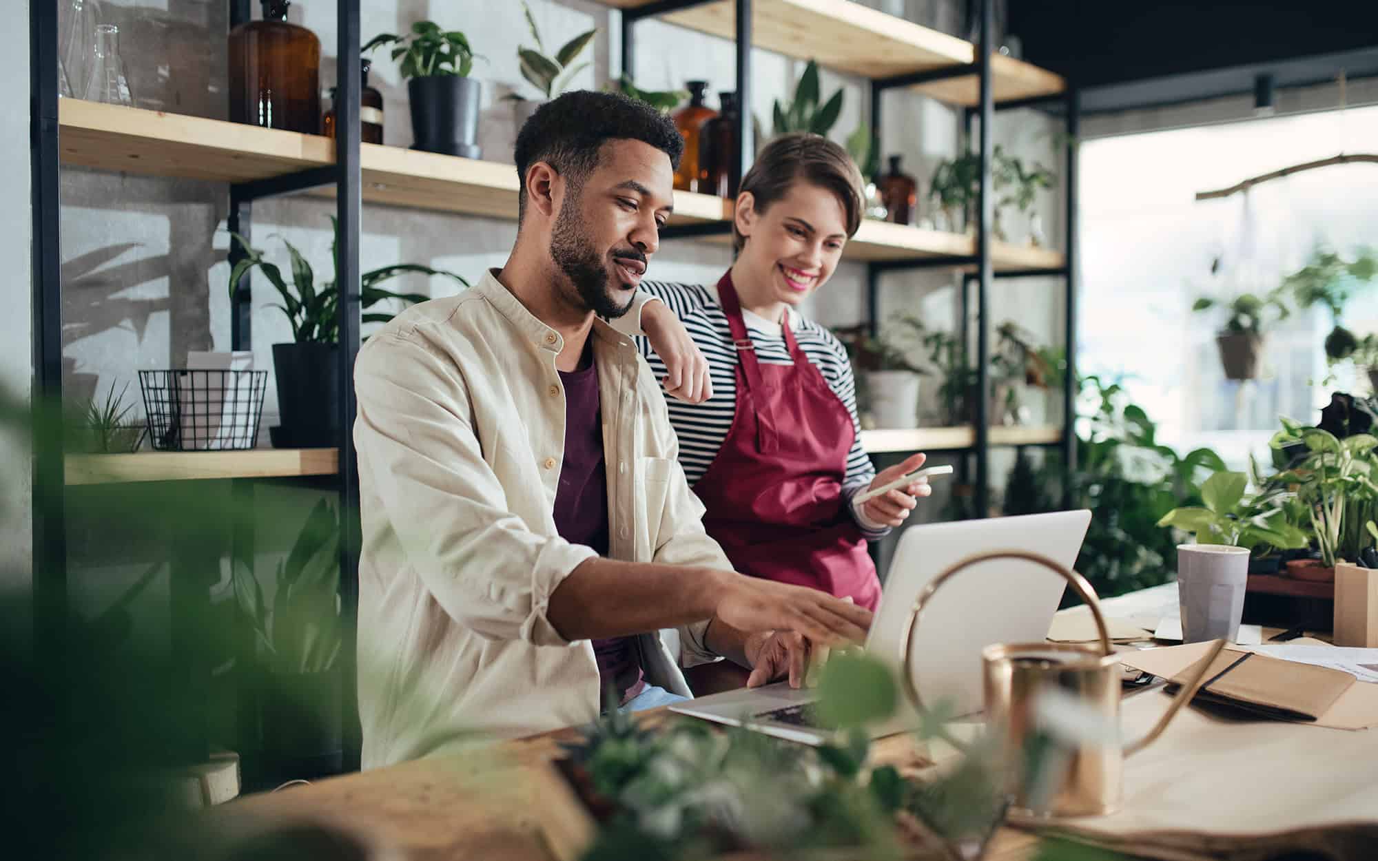 Shop assistants with laptop working in potted plant store, small business concept
