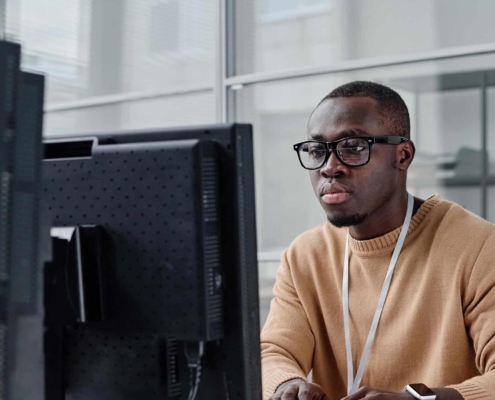 Front view of a man in an orange sweater looking at a computer monitor