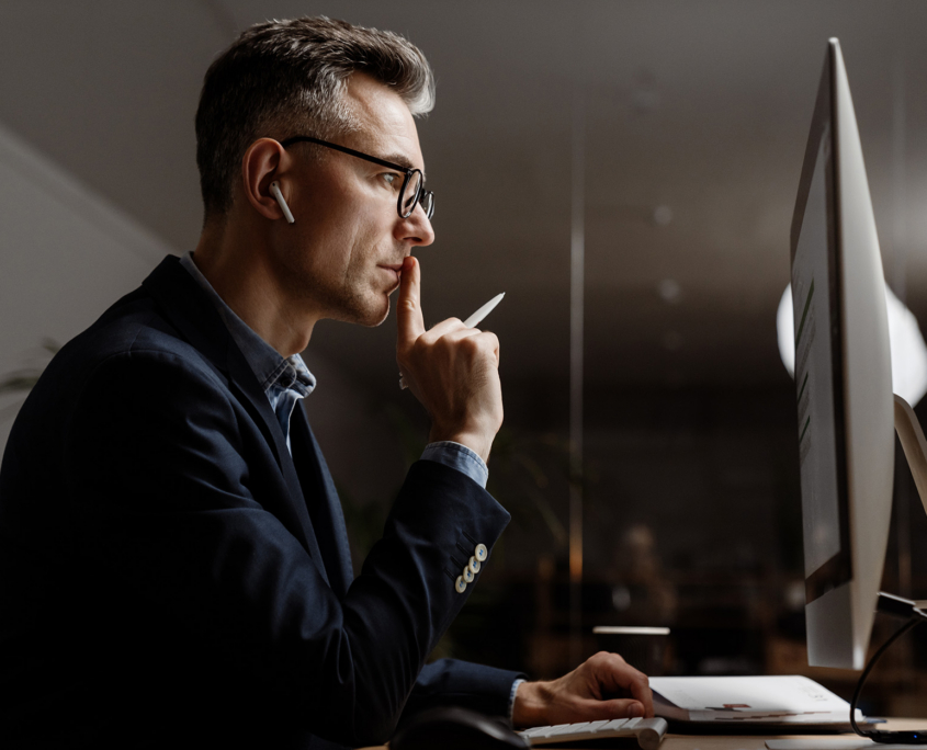 Concentrated grey man in eyeglasses working with computer at office